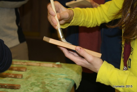 An eighth grade student applies a final layer of polyurethane to her wood pieces. In the class students work with real professional grade tools such palm sanders, table saws and planners. Photo by Sarah Harmon