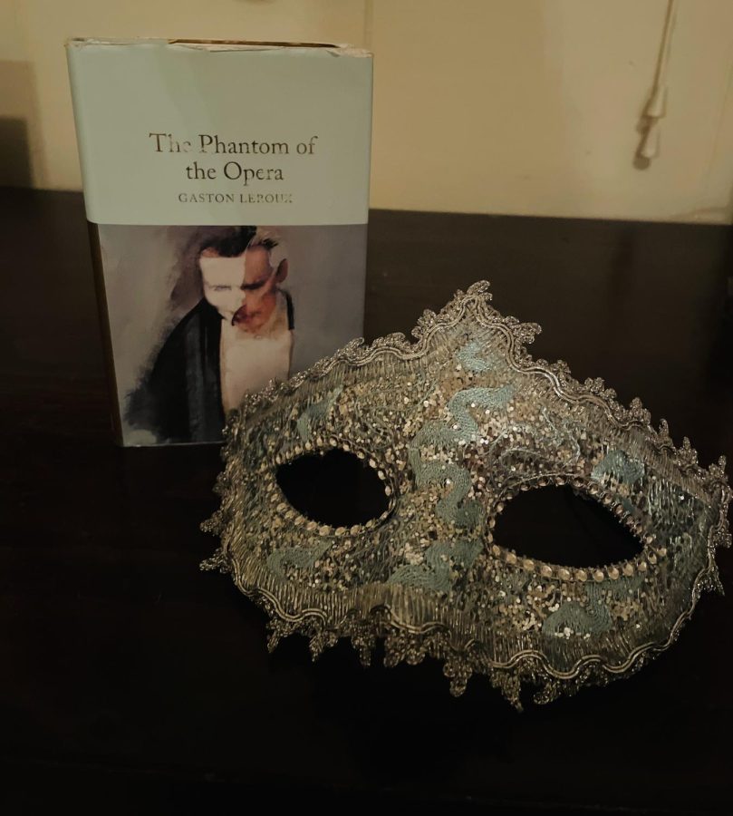 My copy of The Phantom of the Opera next to a masquerade mask to capture the plot and essence of Phantom.