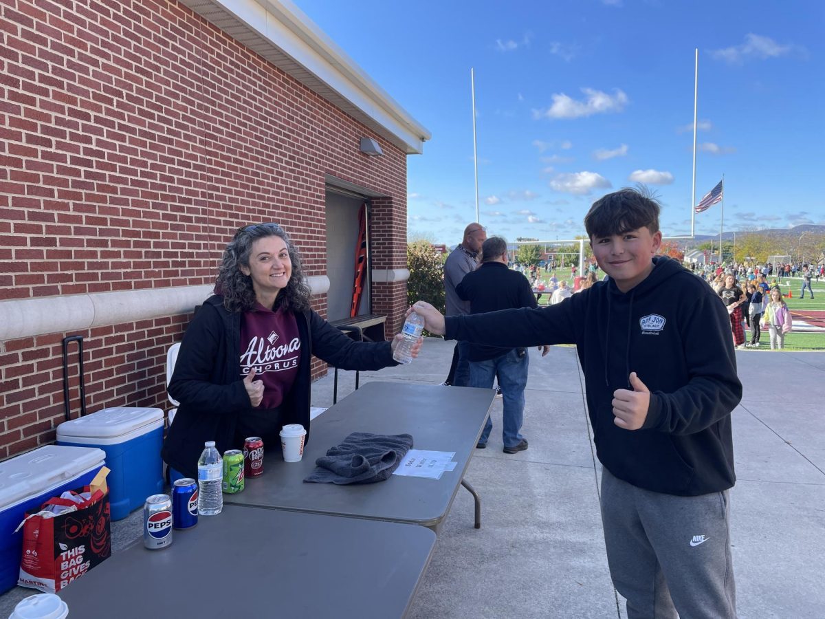 Music teacher Jessica Connell hands eighth grade student Dylan Hawksworth a water bottle, completing the first sale of the day! Many more water bottles were sold at Harvest Day.